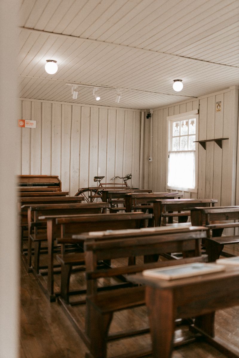 Interior of an old wooden classroom with benches, desks, and a vintage piano, conveying a nostalgic educational setting.