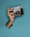 一只透过撕破的蓝色纸背景的手握着一台经典老式相机