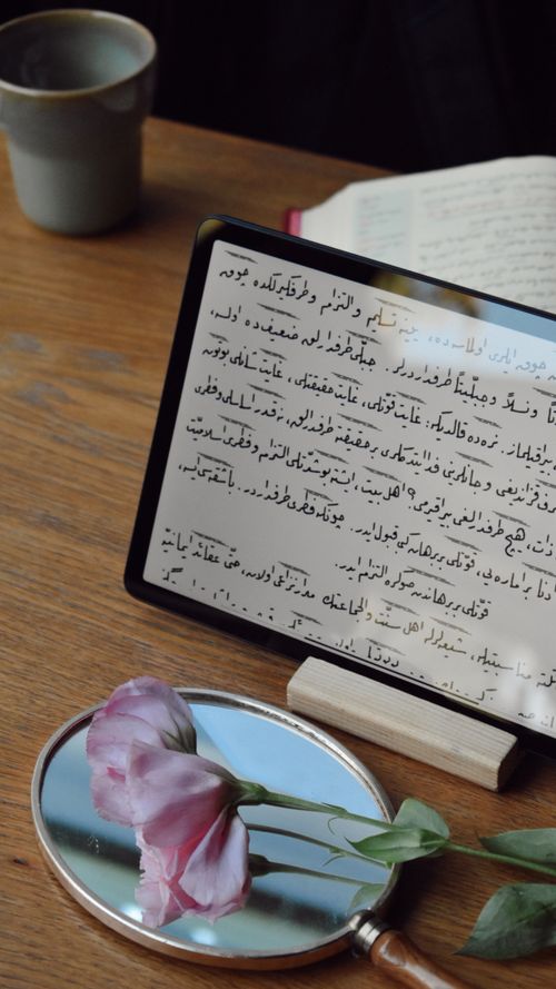 Free A wooden desk with a tablet displaying text, coffee, and a pink flower near a mirror. Stock Photo