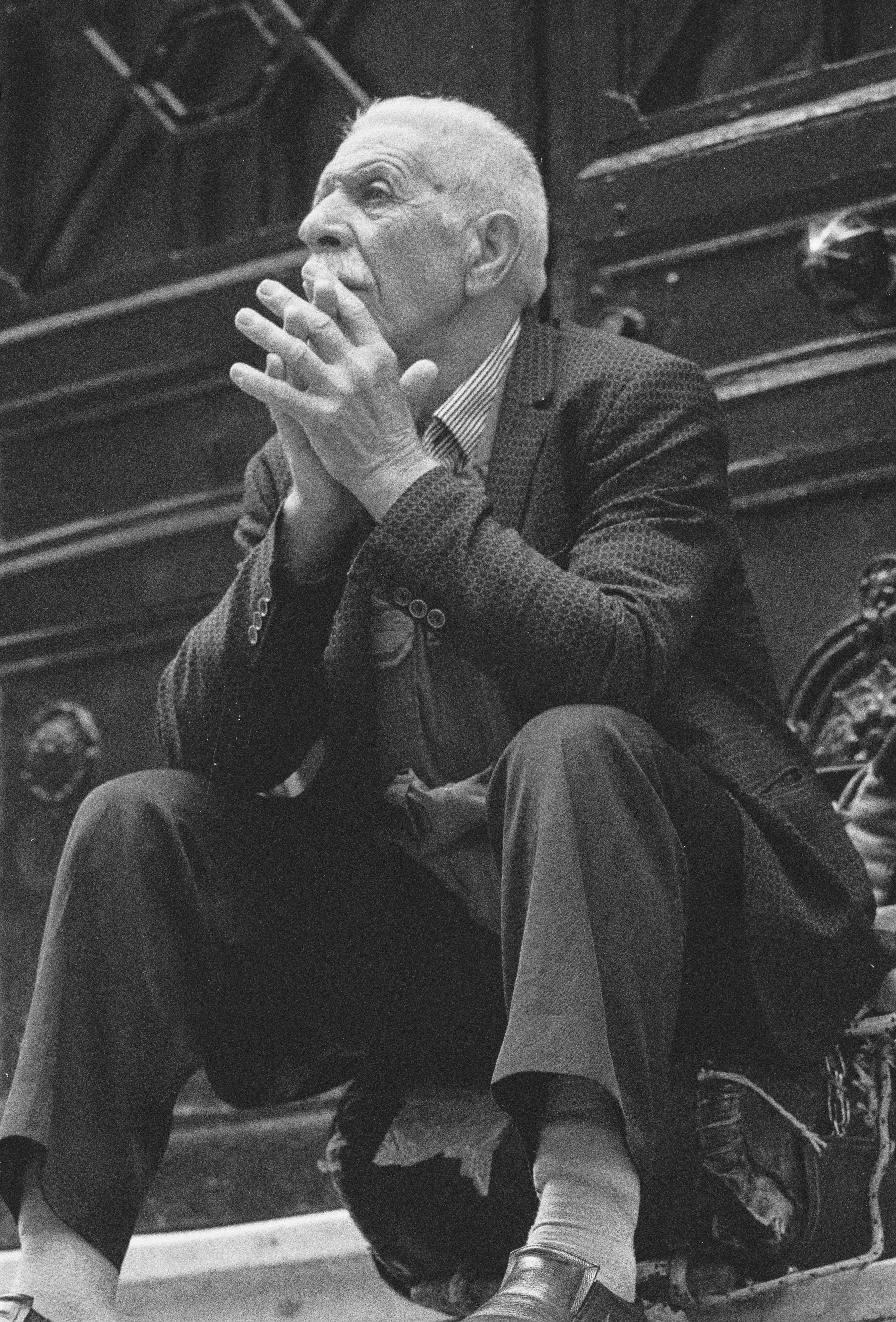 Black and white portrait of an elderly man sitting thoughtfully outdoors.