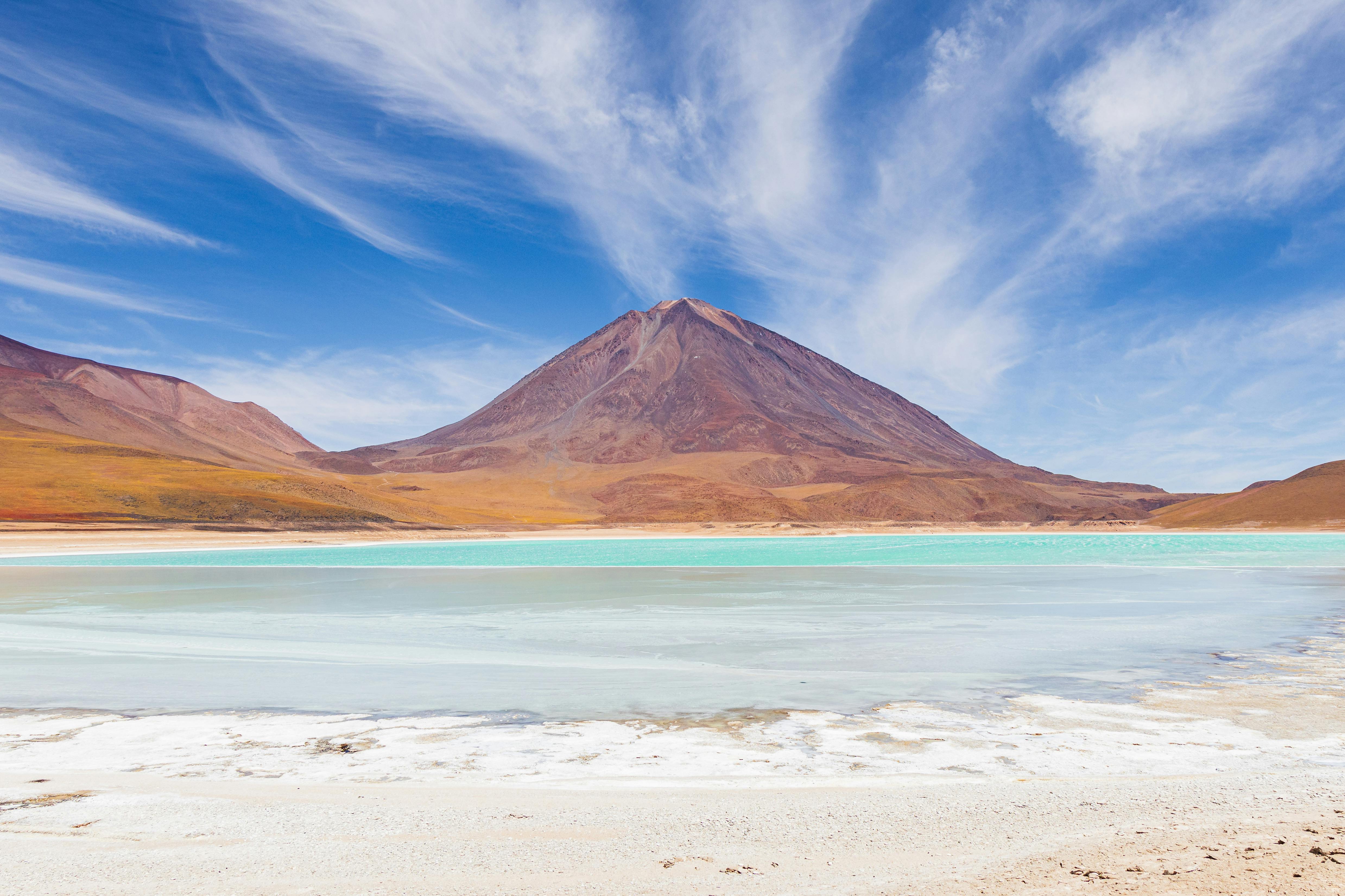 A stunning view of a volcanic mountain overlooking a serene turquoise lake under a clear blue sky.