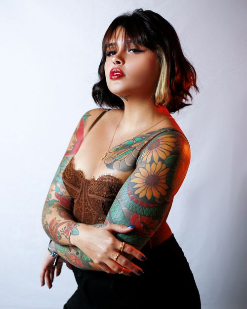 Free Stylish portrait of a tattooed woman showcasing vivid body art and a confident pose in studio lighting. Stock Photo