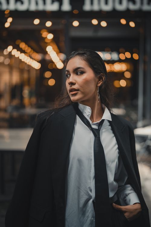 Free Fashionable woman in black suit outdoors with warm city bokeh lights creating a modern and elegant vibe. Stock Photo