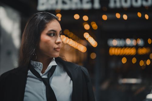 Free Elegant woman in a black suit stands confidently in urban Guadalajara, Mexico with warm bokeh lights in the background. Stock Photo