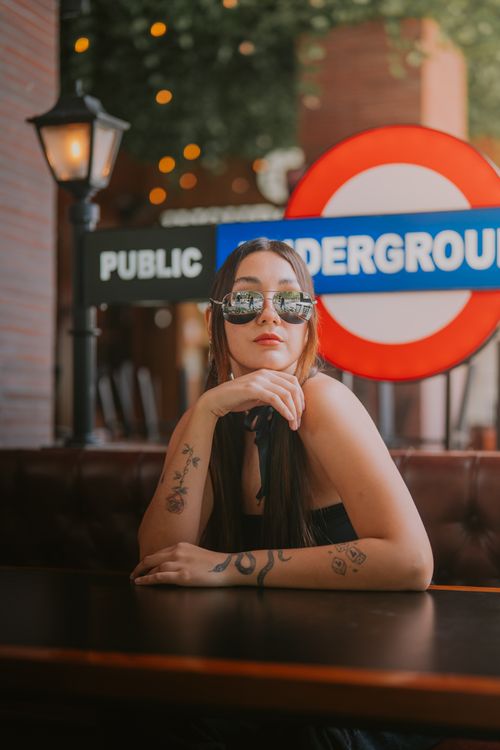 Free Trendy woman with tattoos in a café with a London-style sign backdrop. Stock Photo