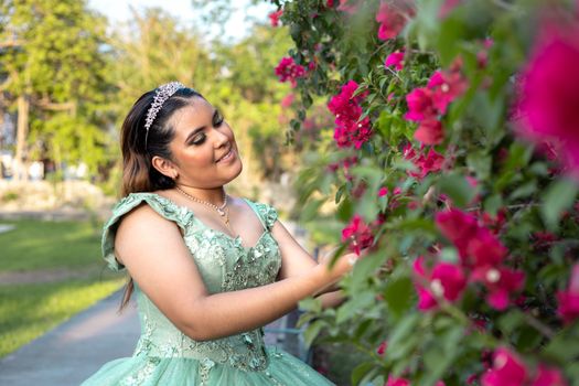 A young woman in a green dress and tiara enjoys a sunny day in a flowering garden.