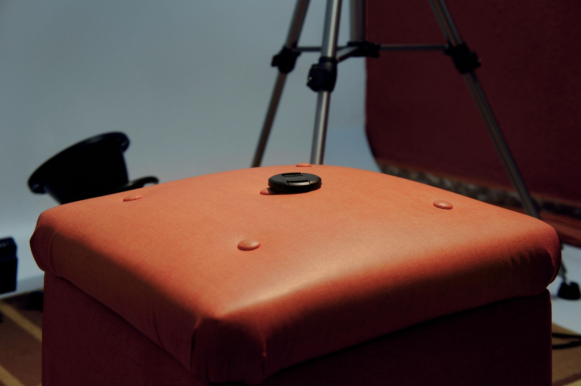 Focus on brown ottoman with camera lens cap in indoor studio setup, no people visible.