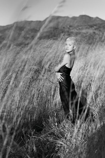 Stylish woman with short hair poses in tall grass, embracing nature's beauty.