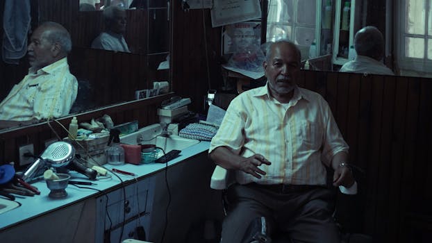 An elderly man sits in a classic barber shop surrounded by vintage grooming tools.