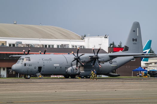 Canadian military transport aircraft on the runway at airport terminal with crew on ground.