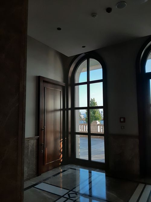 Free A hallway featuring large sunlit windows casting reflections on the marble floor, showcasing elegant interior design. Stock Photo