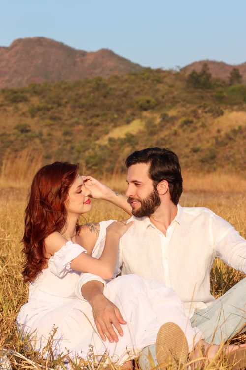 Free Romantic couple enjoying a sunny day outdoors in a field with scenic mountain views. Stock Photo
