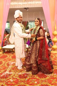 A happy couple in traditional Indian attire during their wedding ceremony indoors.