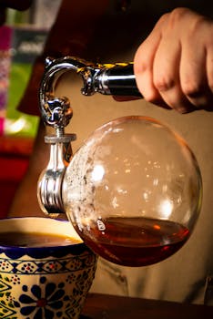 Hand pouring coffee from siphon into cup, showcasing luxury brewing process.
