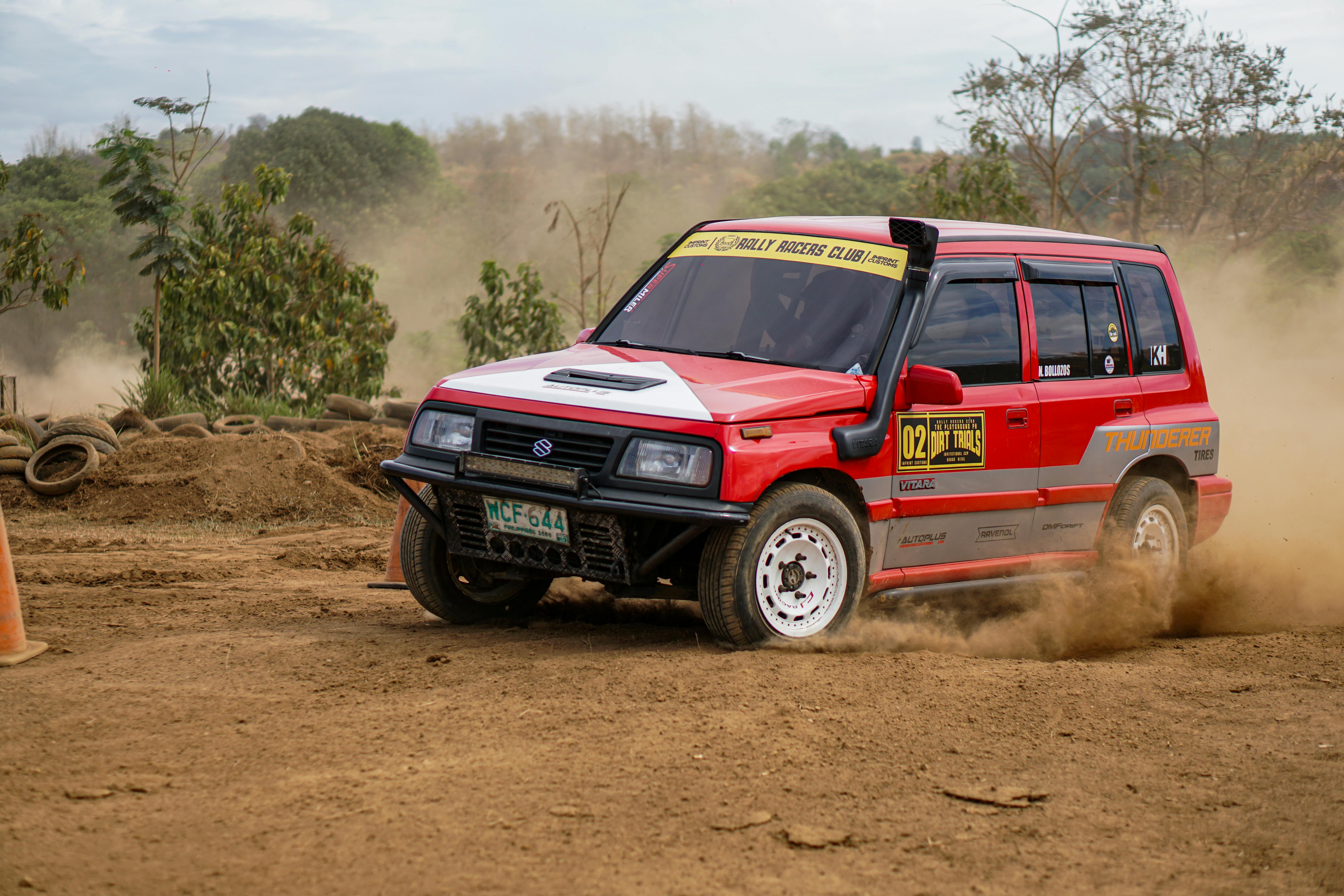 Exciting off-road rally event with a red car racing through a dusty track, showcasing speed and agility.