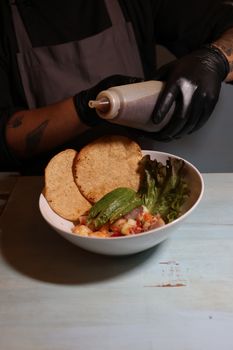 Chef adds sauce to a gourmet dish with fresh tortillas, avocado, and greens.