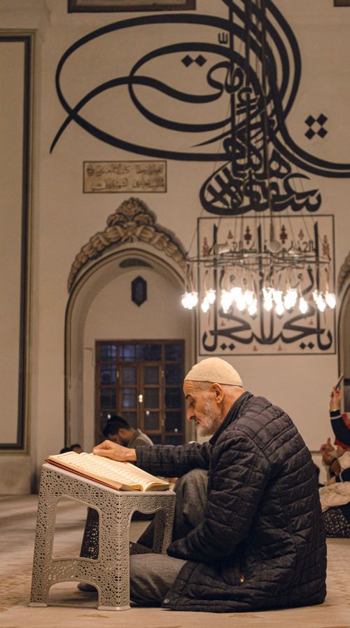 Free An elderly man reads the Quran in a mosque in Bursa, Türkiye, showcasing spirituality and tradition. Stock Photo