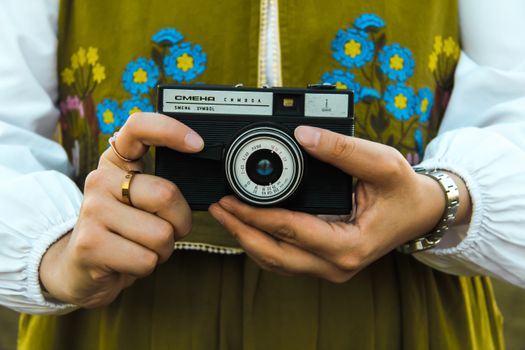 Close-up of hands holding a vintage camera with an embroidered floral background.