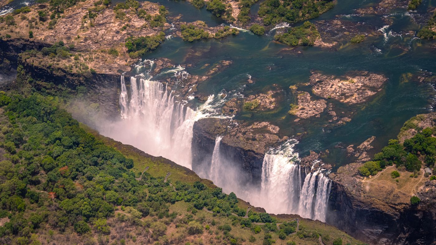 Aerial view of Victoria Falls on the Zambezi River, Zimbabwe, with mist rising from the gorge amid lush green surroundings