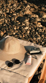 Retro beach setup with hat, sunglasses, and camera on a rocky shore, bathed in warm sunlight.