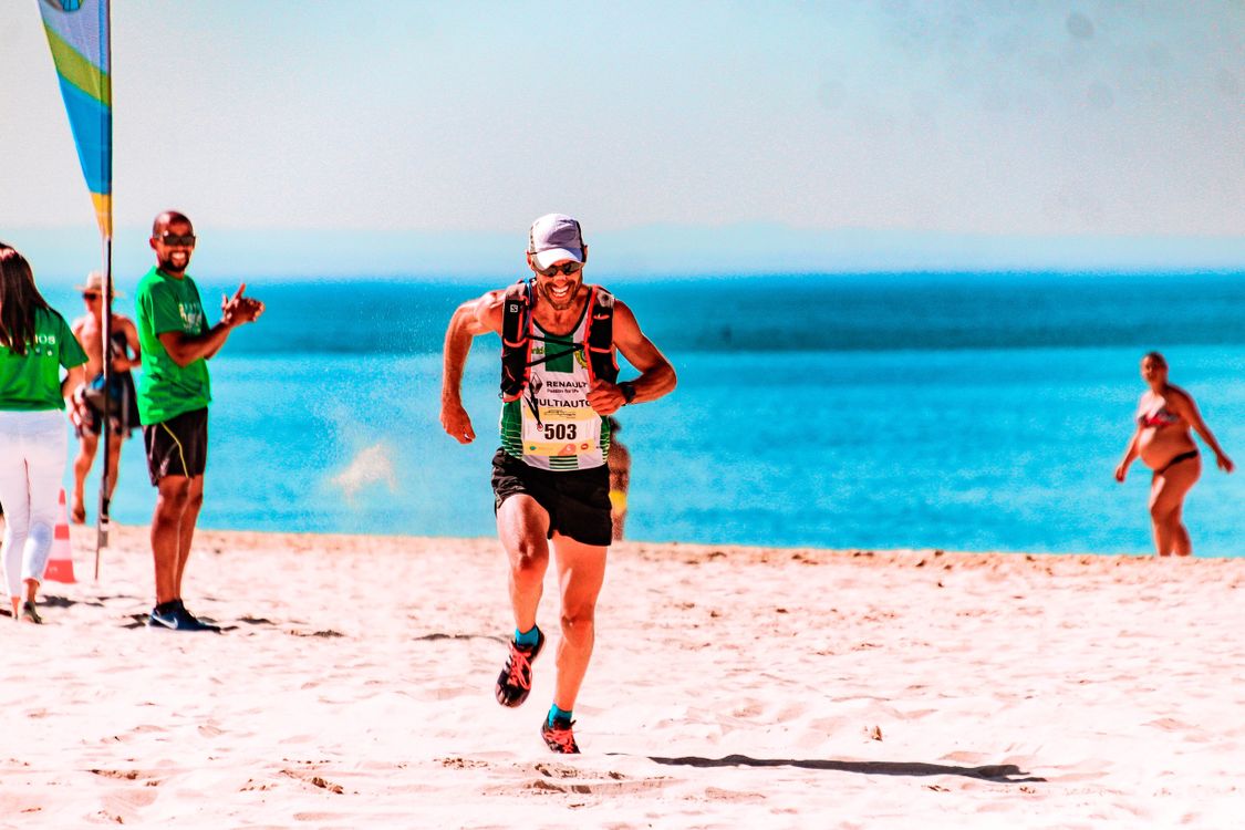 Free Athlete running a race on a sunny beach by the ocean, showcasing determination and fitness. Stock Photo