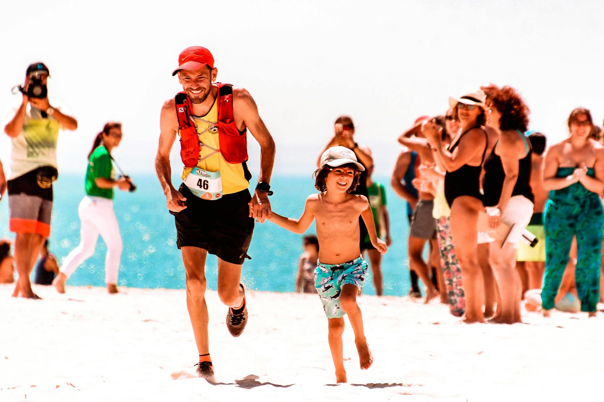 A joyful father and son run on the beach during a lively community event. Perfect summer day.