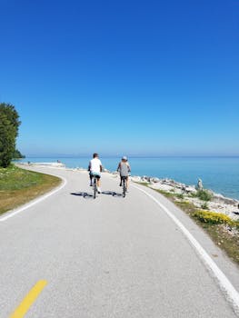 Two cyclists ride along a beautiful coastal path with clear skies and ocean views.