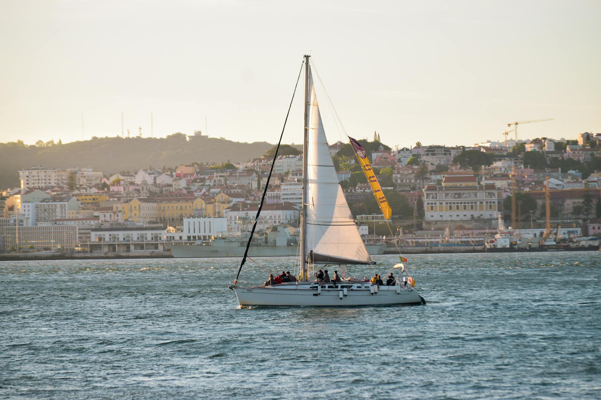 A sailboat cruises along the Lisbon waterfront with a scenic view of the city in the background.