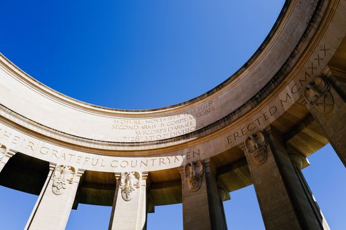 Free Upward view of a neoclassical monument with columns and inscriptions, against a clear blue sky. Stock Photo