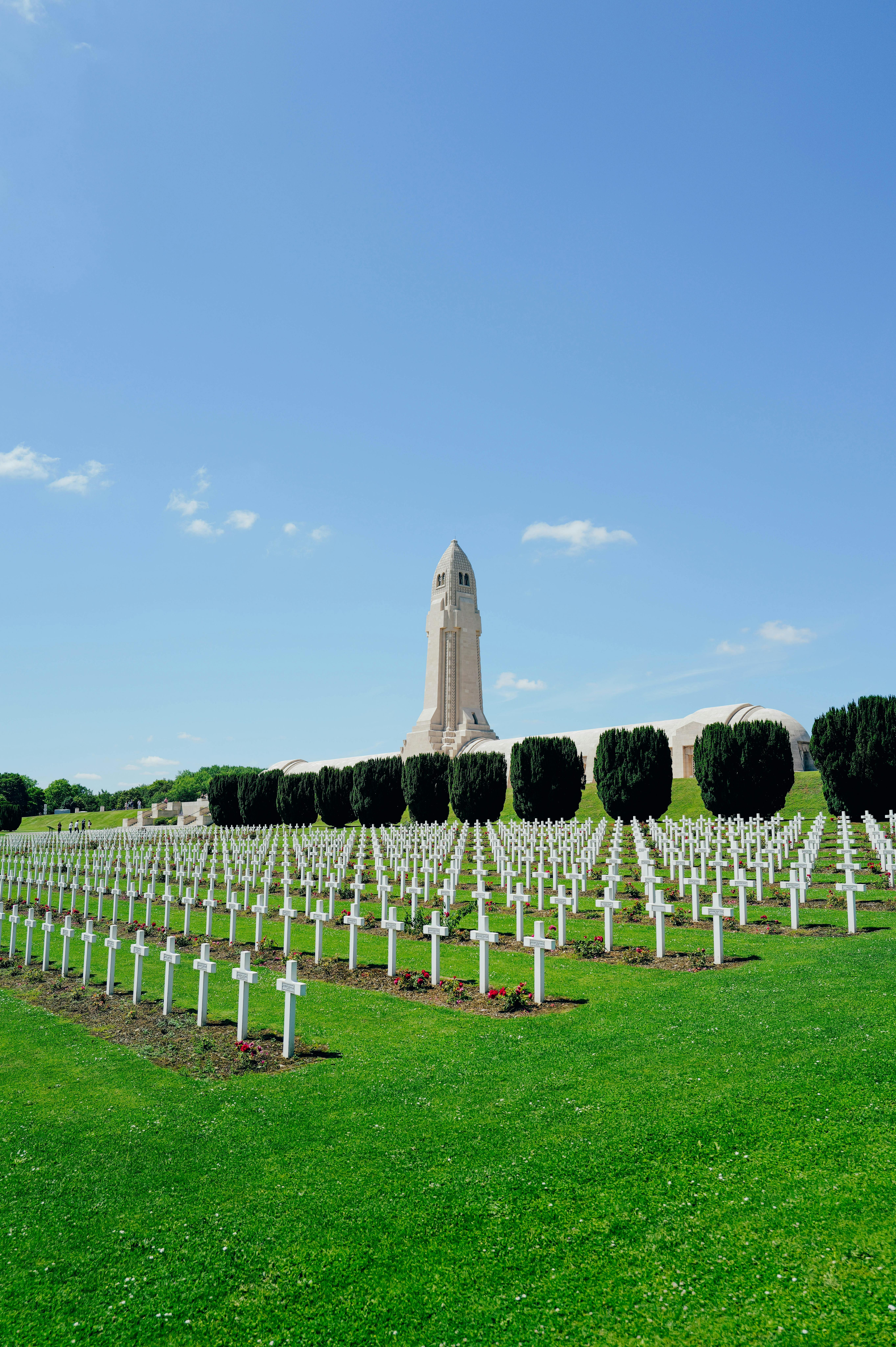 Rows of crosses at Verdun Memorial Cemetery with a distinctive tower under clear skies in summer.