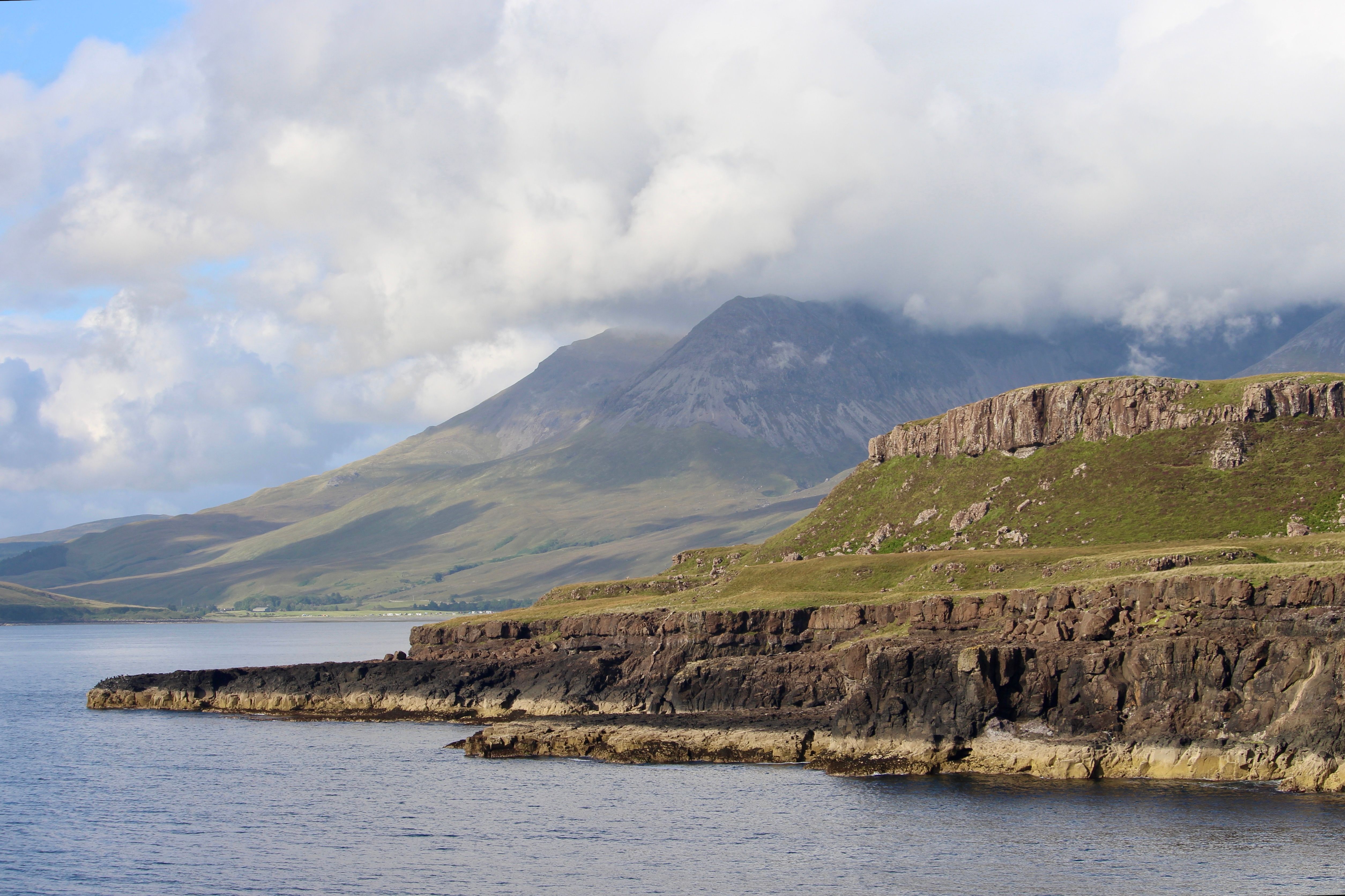 Breathtaking view of coastal cliffs with mountains in the background and summer sky.