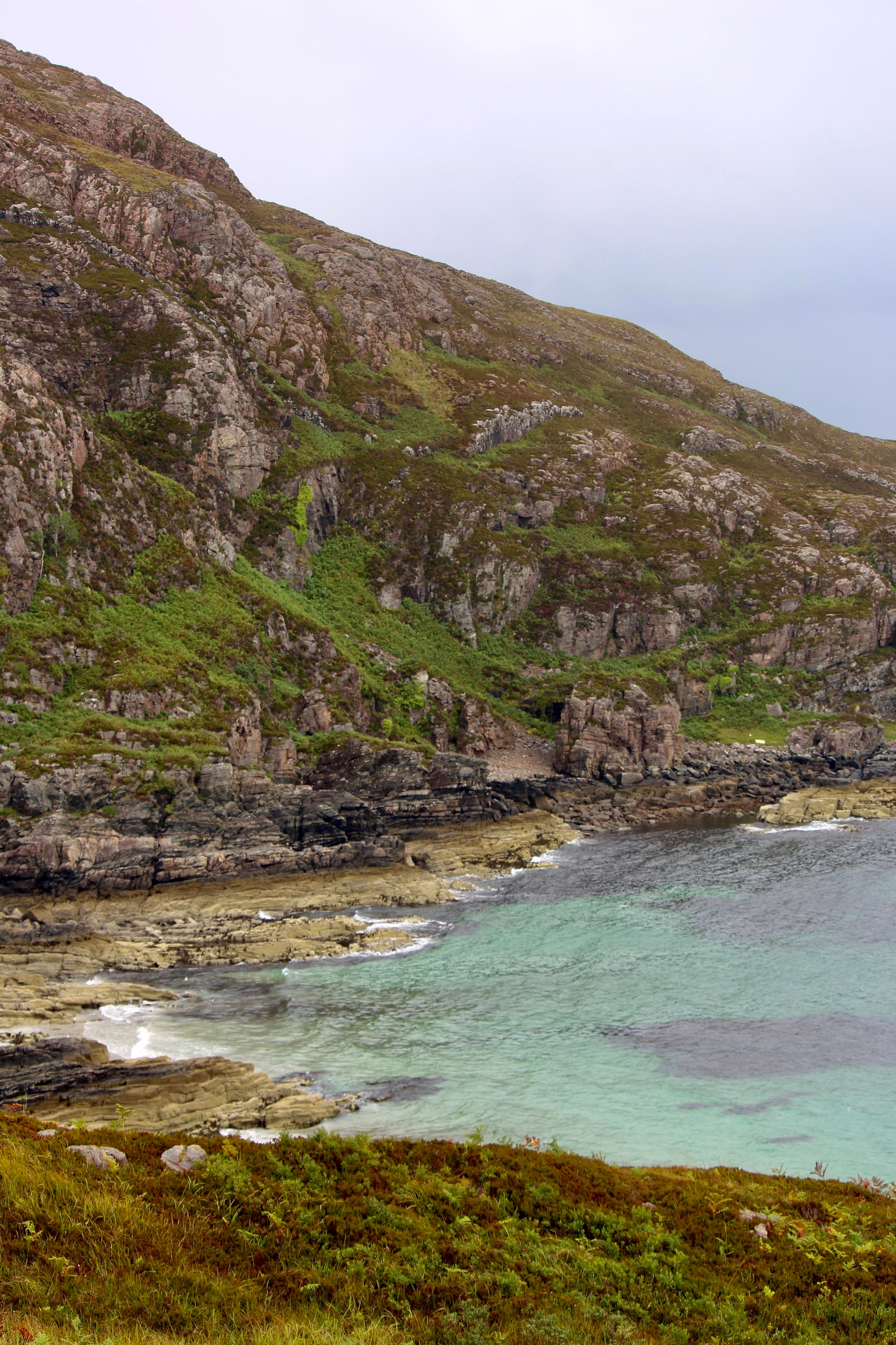 A stunning coastal landscape featuring cliffs and turquoise sea on a cloudy day.