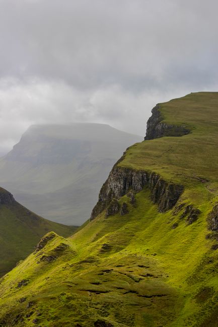 Majestic green cliffs enveloped in mist and clouds, showcasing a dramatic landscape view.