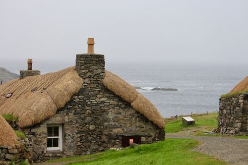 Free Rustic stone houses with thatched roofs overlooking the sea in a rural setting. Stock Photo