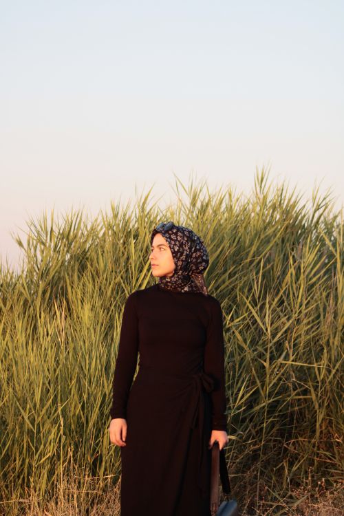 Free Portrait of a woman in a hijab standing in a grassy field during sunset. Stock Photo