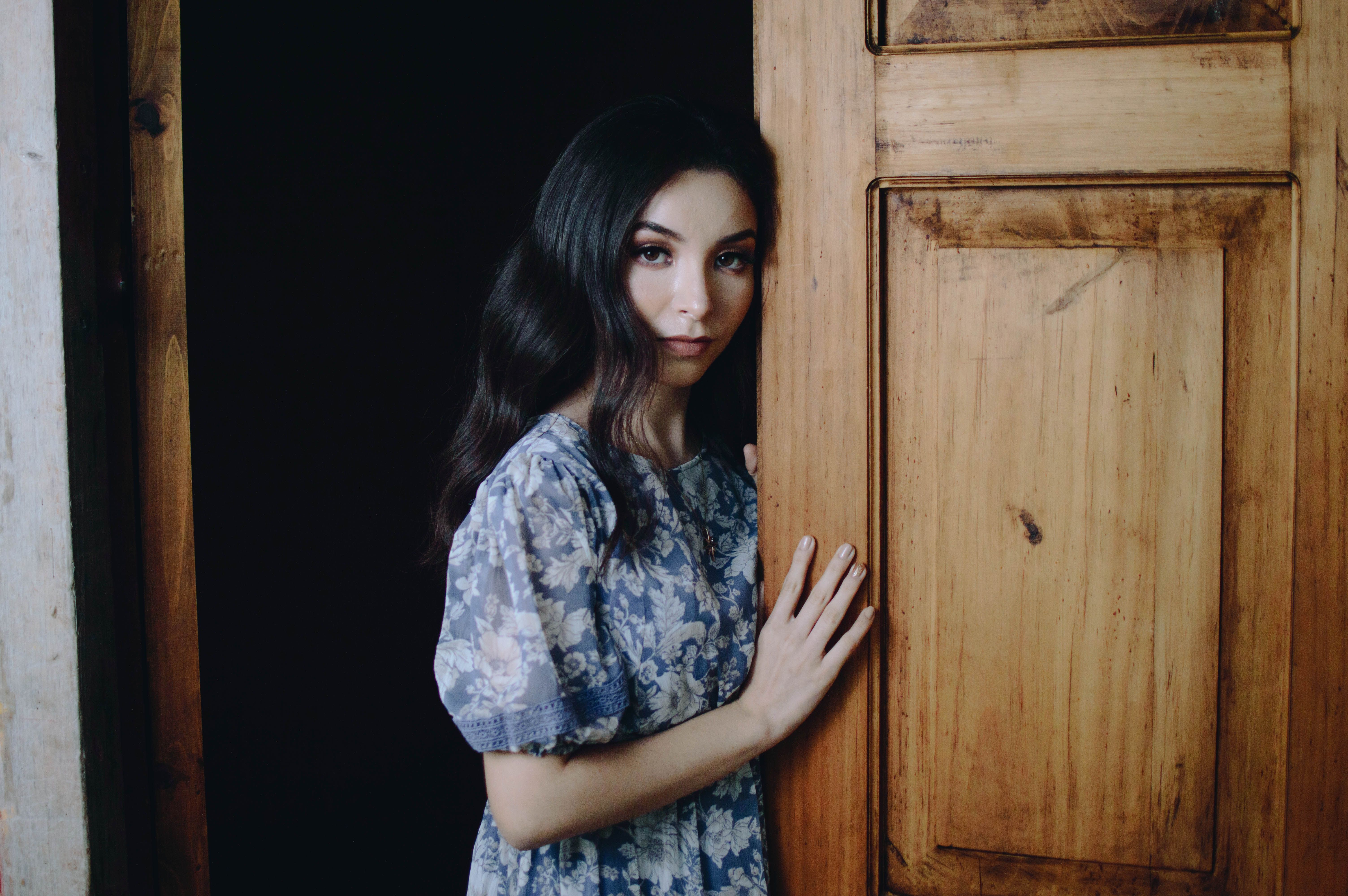 A woman in a blue dress leaning against a wooden door · Free Stock Photo