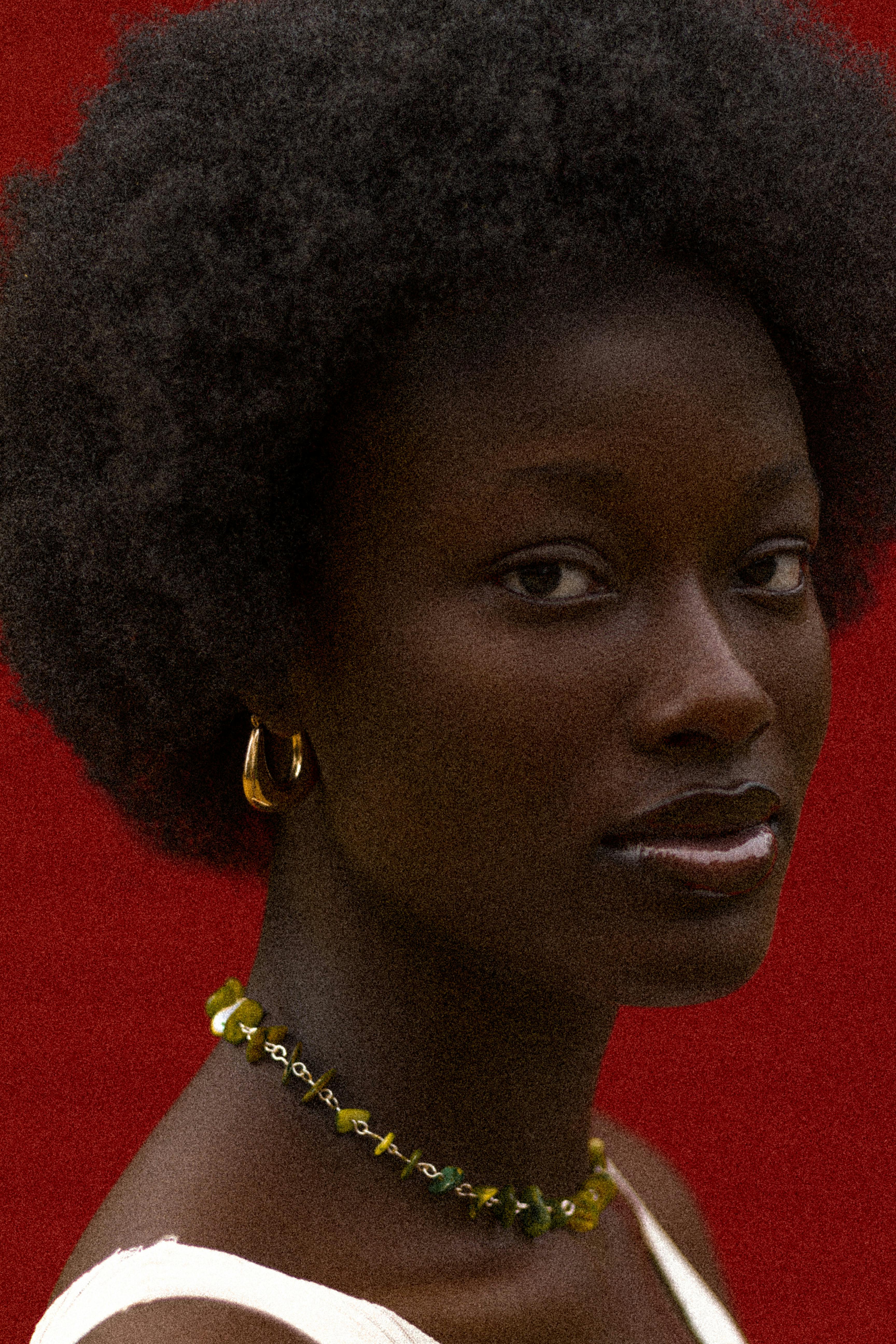 Close-up portrait of a woman with afro hair wearing jewelry against a red background.