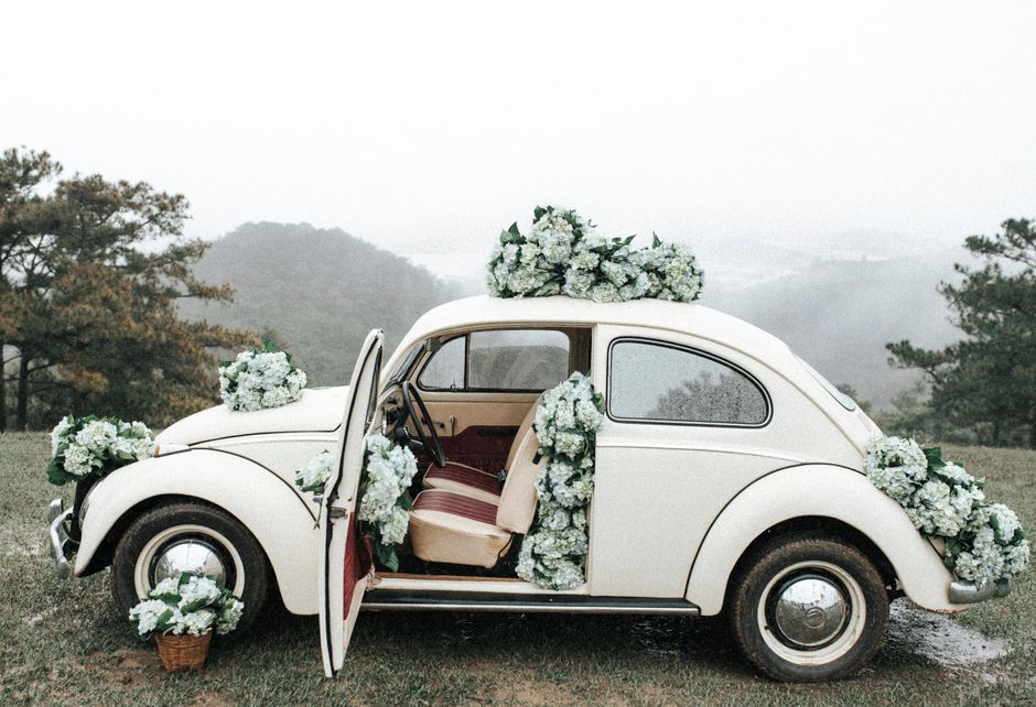 A vintage car adorned with flowers, parked in a misty rural field, capturing a romantic wedding vibe.