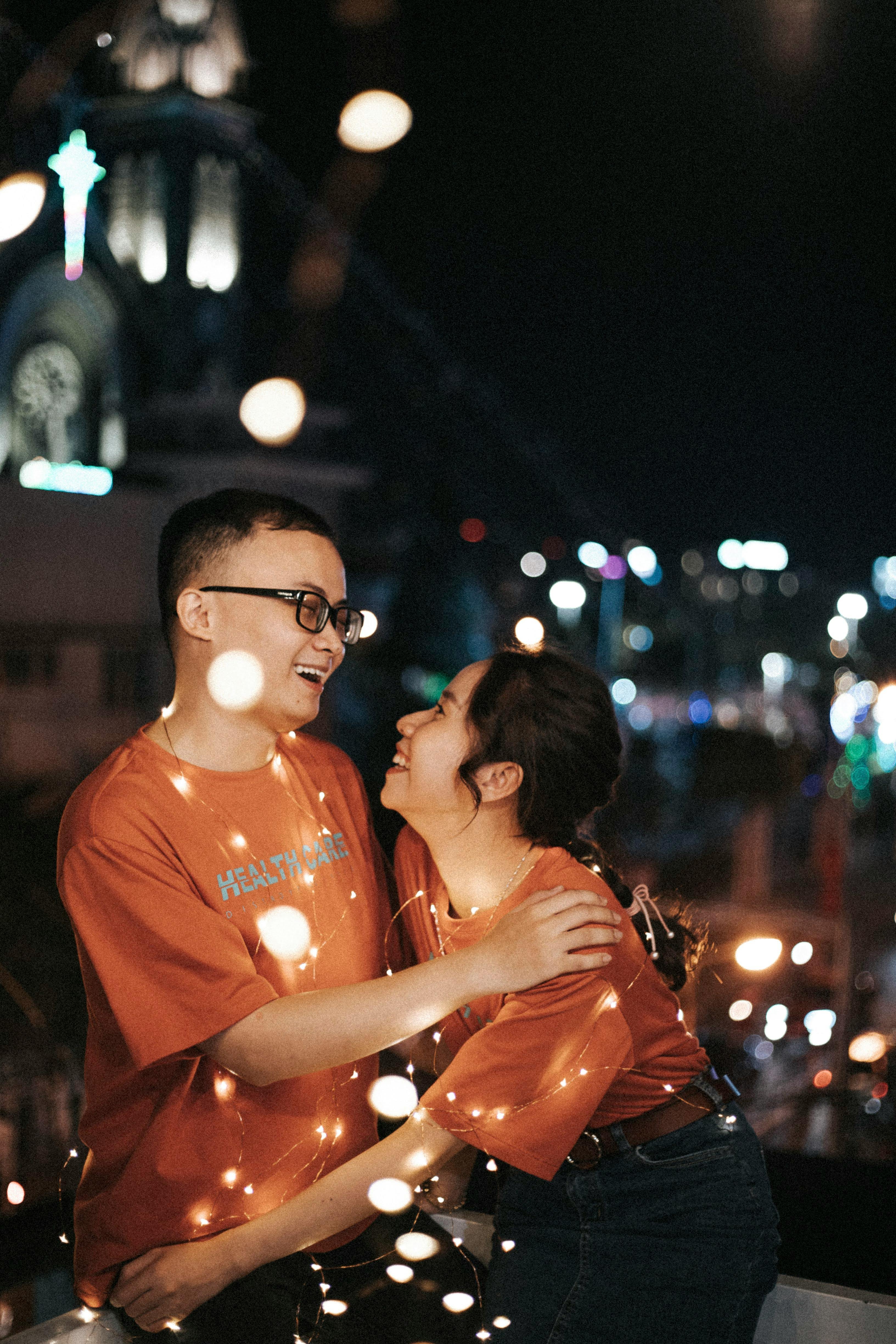 Happy couple sharing a joyful moment wrapped in string lights during a night festival.