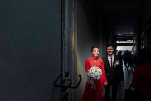 A couple smiling in a dimly lit hallway, holding hands at their wedding ceremony.