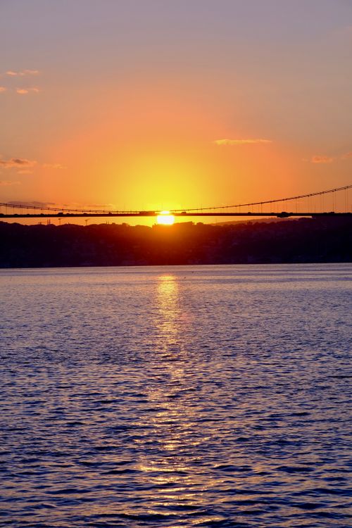 Free A stunning sunset over Bosphorus Bridge reflecting on tranquil waters, showcasing vibrant colors. Stock Photo