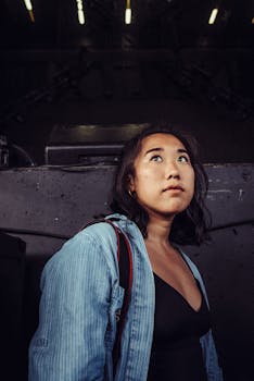 在昏暗的室内，一名穿着休闲装的年轻女子若有所思地抬头望着