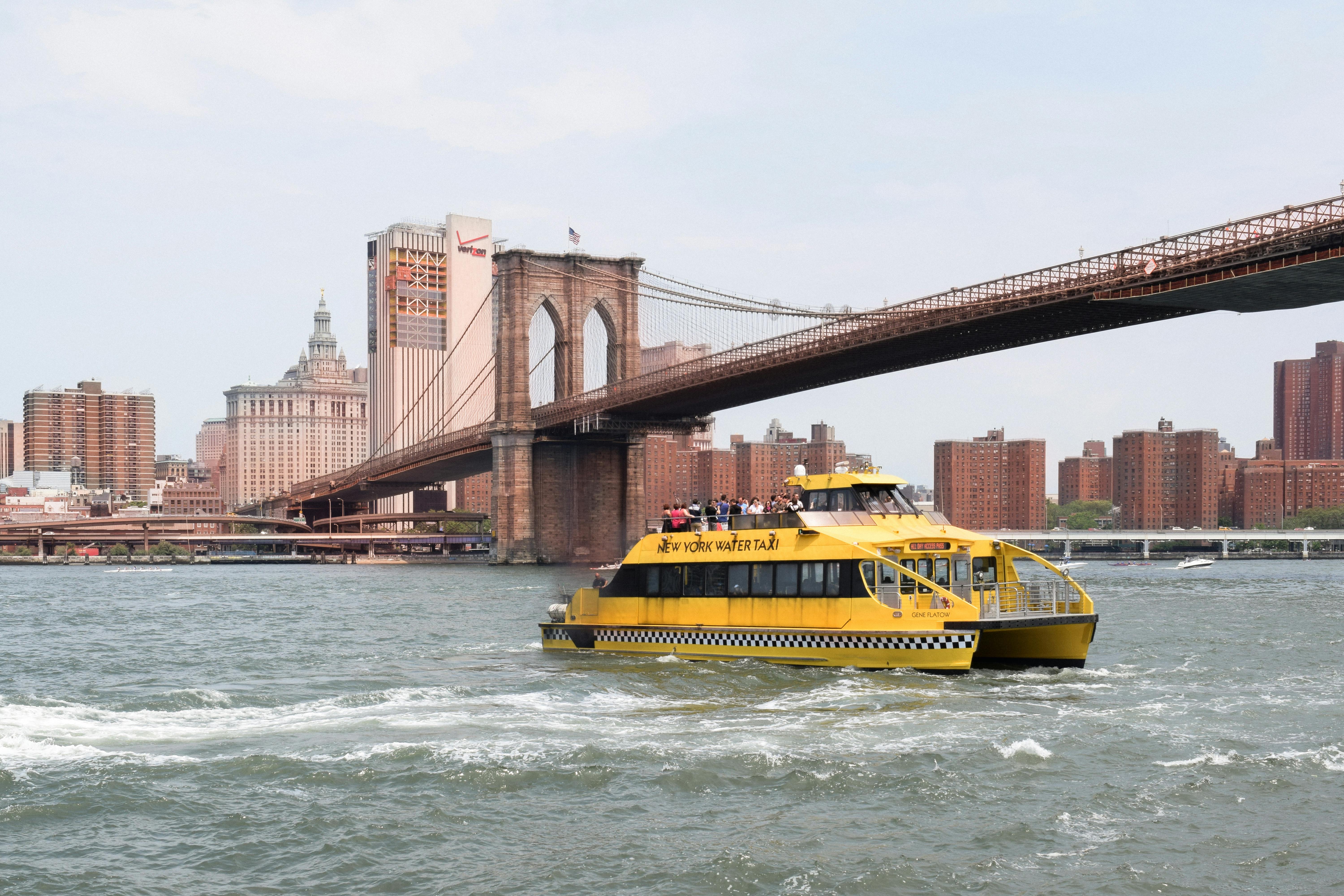 a yellow boat traveling across the water near the brooklyn bridge