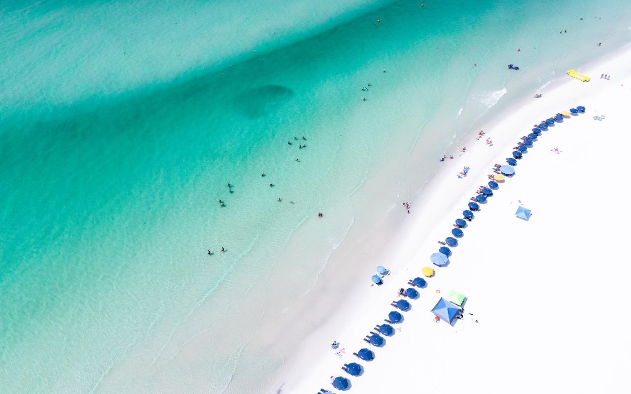 Stunning aerial view of Santa Rosa Beach showcasing turquoise waters and colorful umbrellas, perfect summer destination.