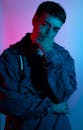 一名穿着牛仔夹克的男子在鲜艳的红蓝灯光下，若有所思地摆着姿势