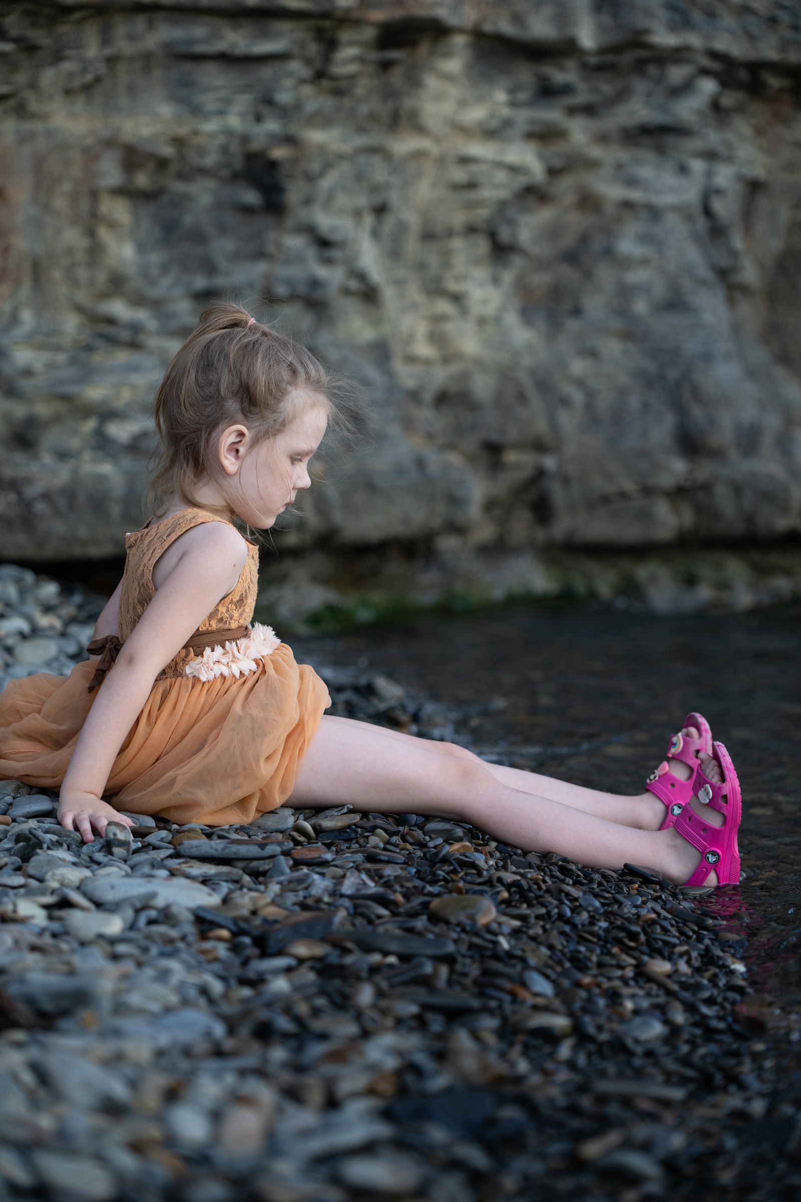 A little girl sitting on the rocks in a dress · Free Stock Photo
