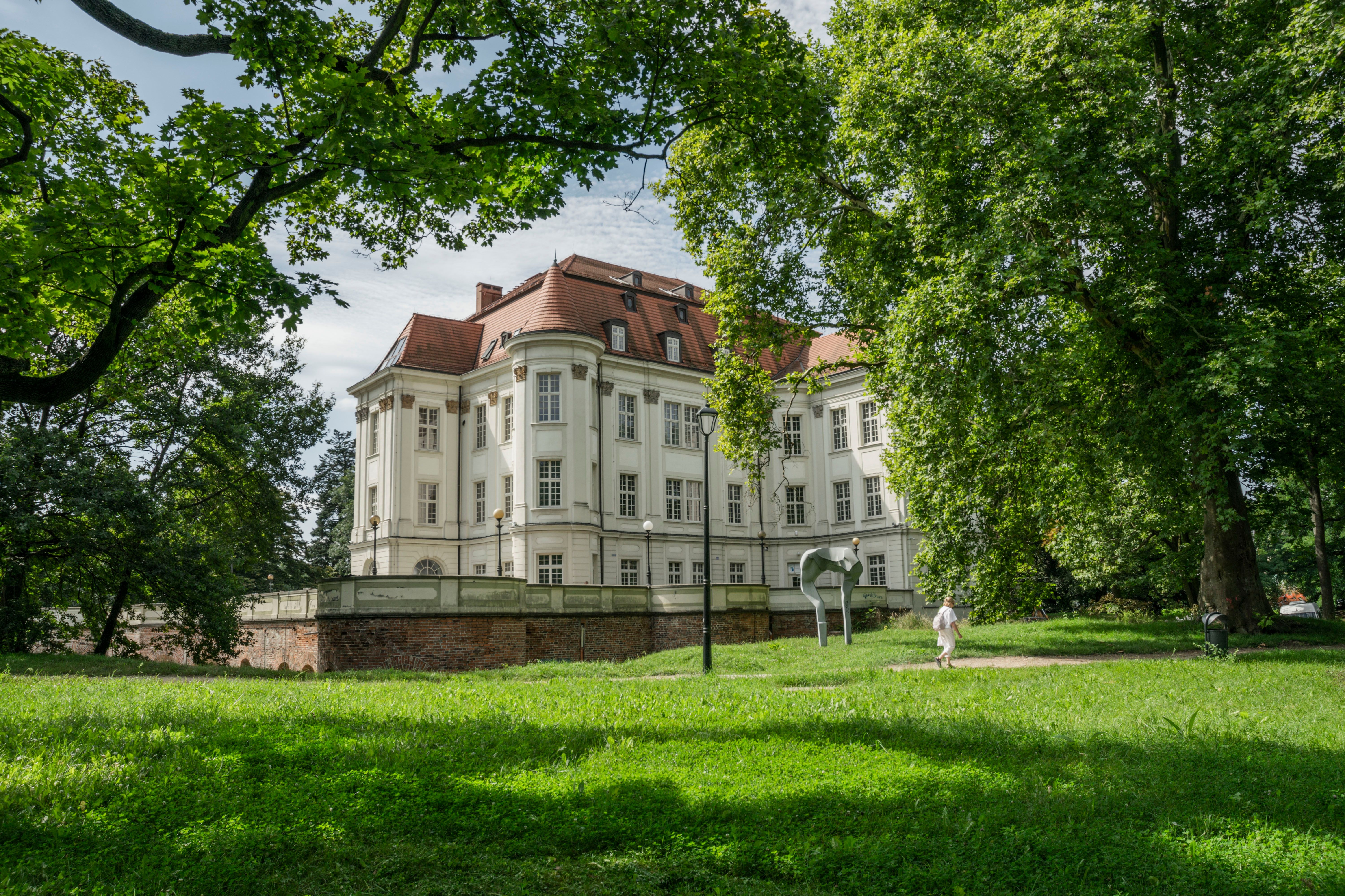 A beautiful historical mansion surrounded by lush greenery and vibrant gardens in Wrocław, Poland.