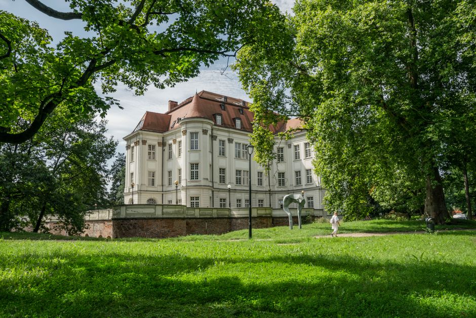 A beautiful historical mansion surrounded by lush greenery and vibrant gardens in Wrocław, Poland.