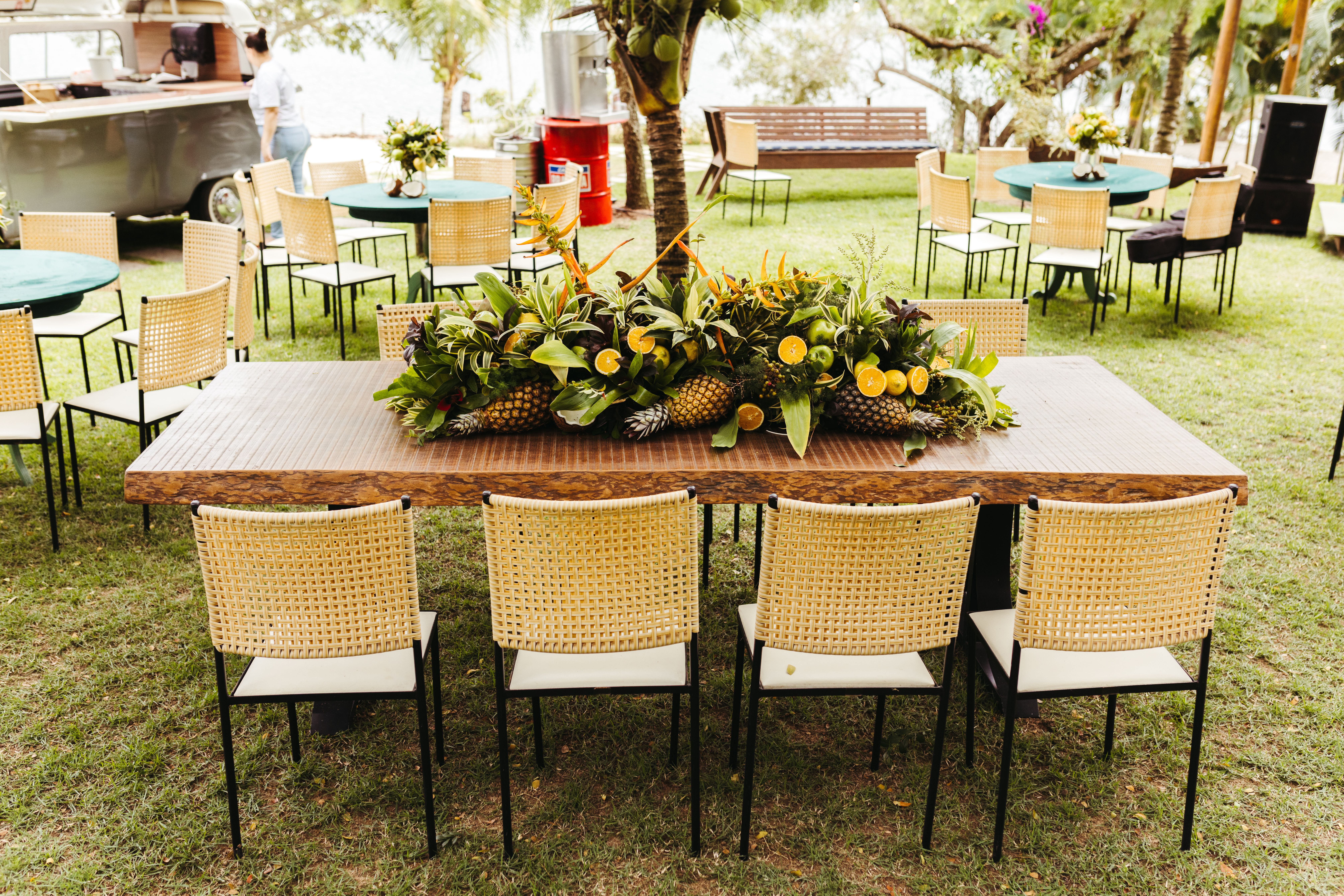 A festive outdoor dining setup featuring tropical fruit decor on a wooden table and woven chairs.