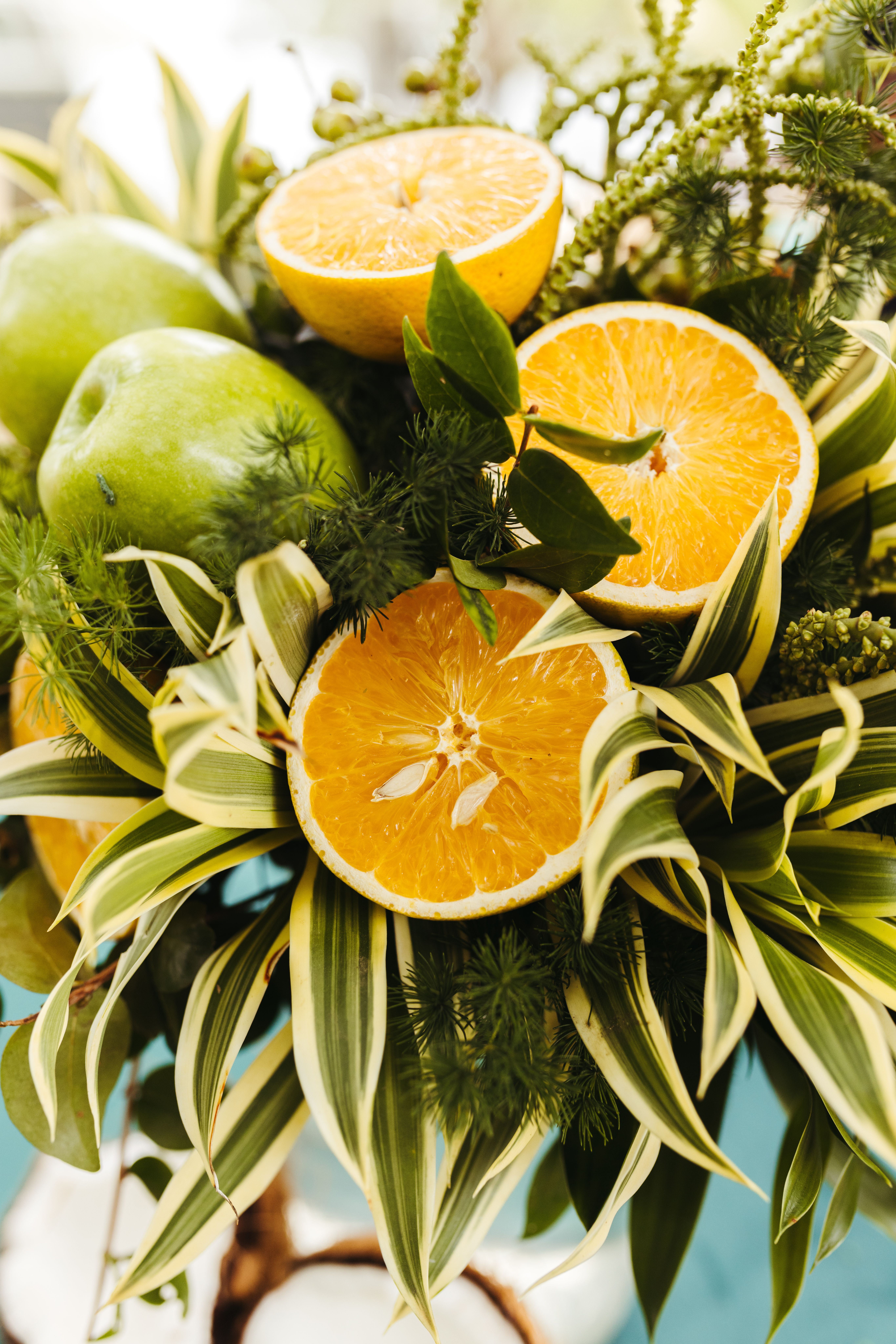 A colorful still life of oranges, apples, and tropical leaves, showcasing freshness.